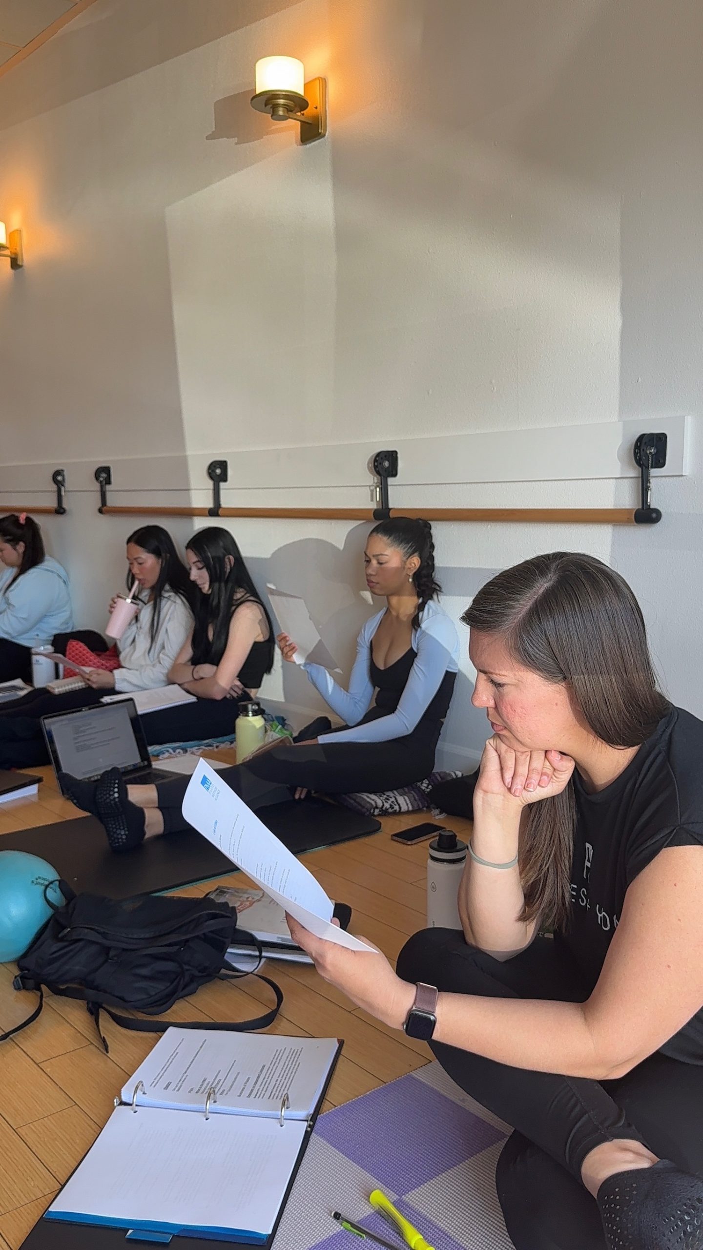 Pilates Teacher Training students reading notes on their mats