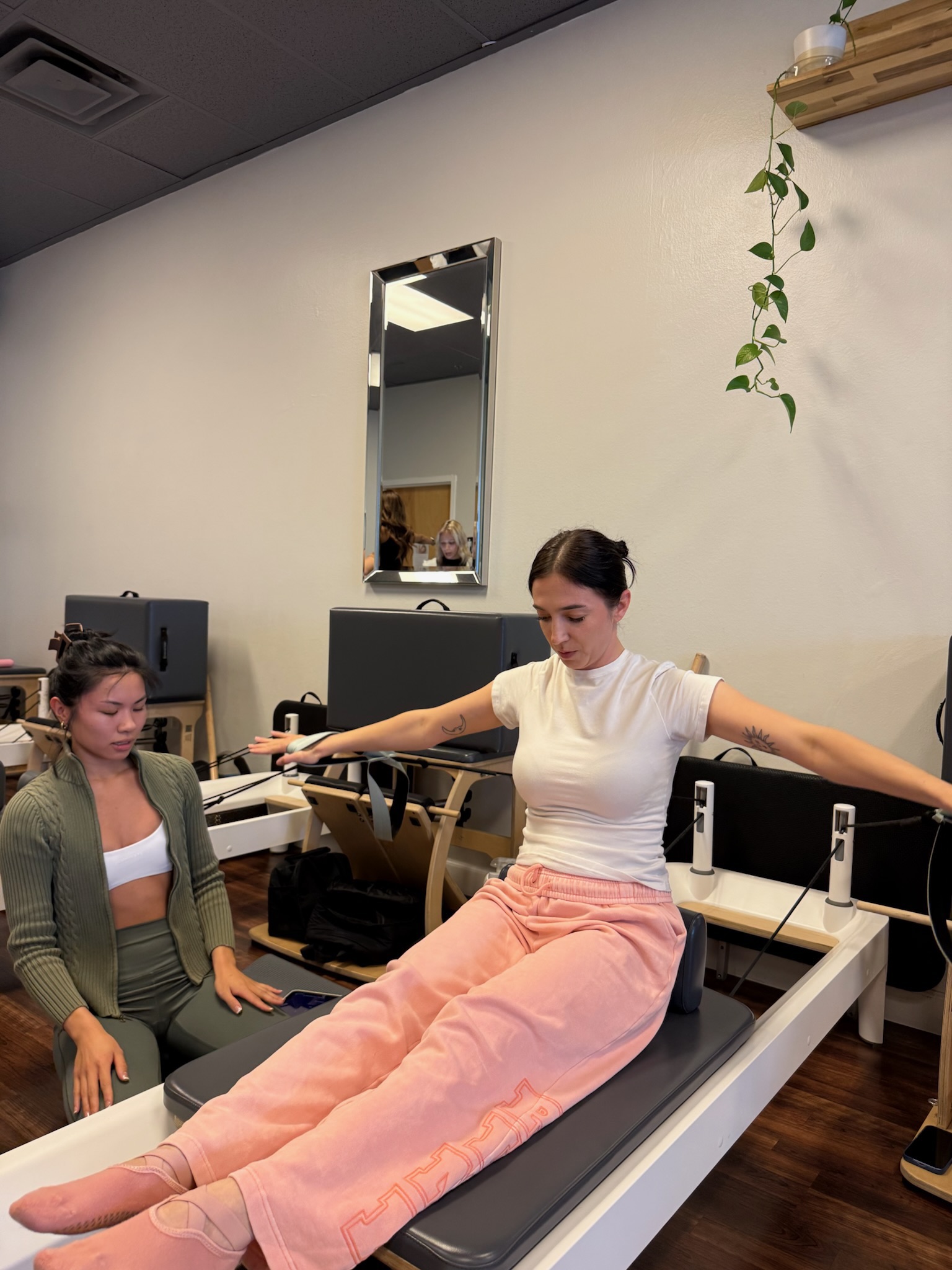 Pilates Teacher Training student practicing seated arm series on the reformer while other student teaches